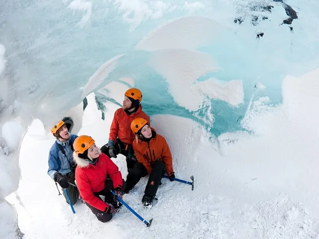 Four hikers with ice axes resting inside a blue ice cave