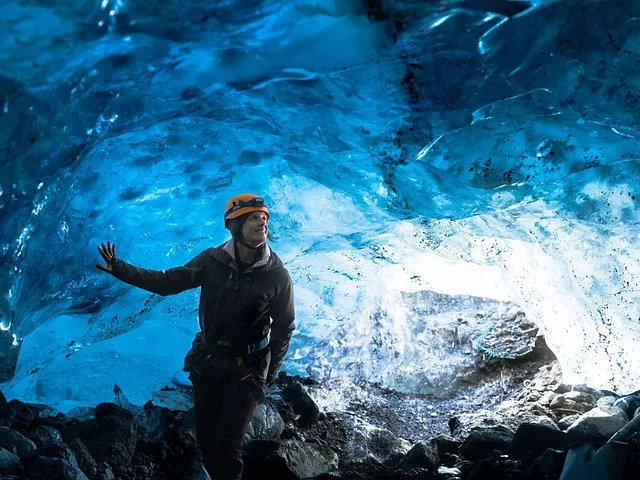 Woman in orange helmet standing inside a glowing blue ice cave on Sólheimajökull Glacier.