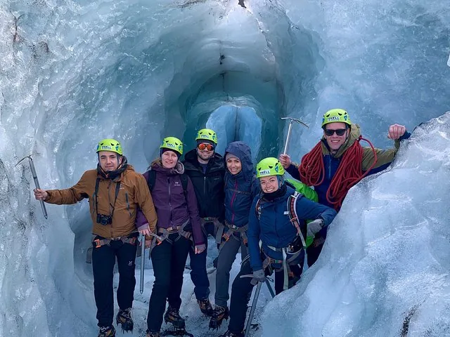Group of six hikers posing inside a blue ice cave.