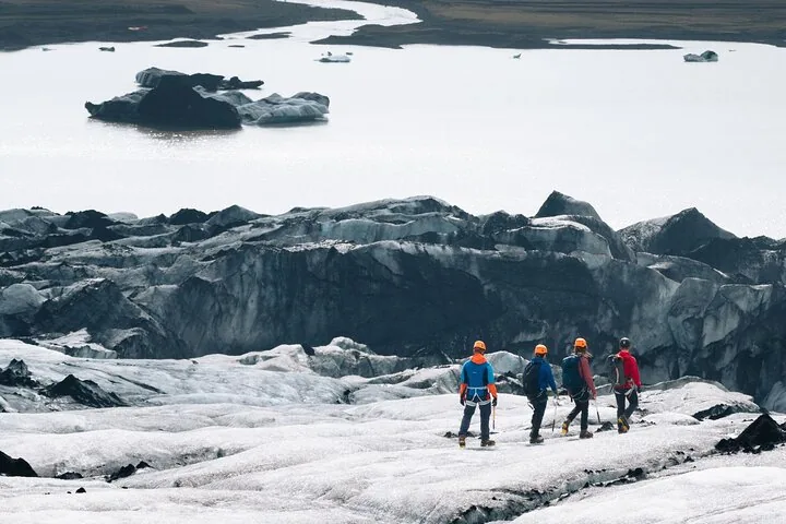 Vier Wanderer auf dem Sólheimajökull-Gletscher, im Hintergrund eine Gletscherlagune.