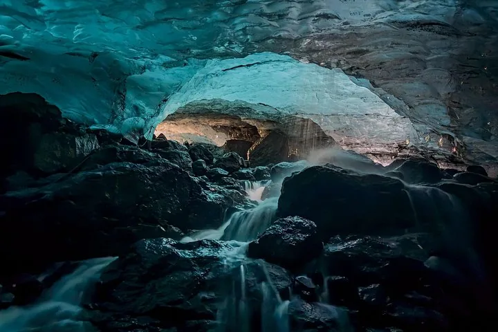 De l'eau s'écoule sur des roches sombres à l'intérieur d'une grotte de glace bleue à couper le souffle sur le glacier Sólheimajökull.