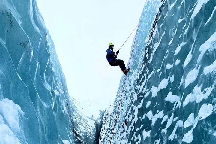 Person rappelling down a steep, narrow glacier crevasse.